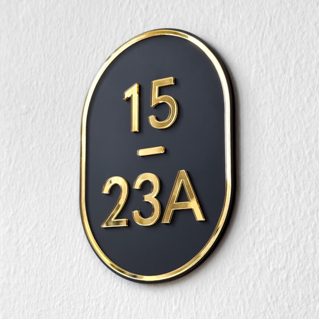 Blissbies material sample with gold mirror acrylic numbers 15 and 23A on a black acrylic oval base